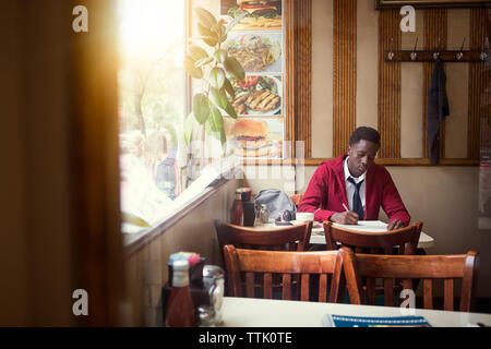 Teenager in Schuluniform Schreiben beim Sitzen im Restaurant Stockfoto