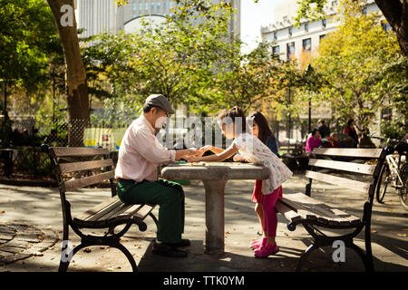 Seitenansicht der Mädchen spielen checkers Spiel mit grossvater am Tisch in Park Stockfoto