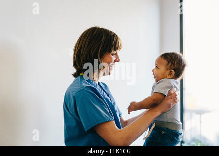 Lächelnd weibliche Arzt Durchführung baby boy, während man durch die Fenster im Krankenhaus Stockfoto