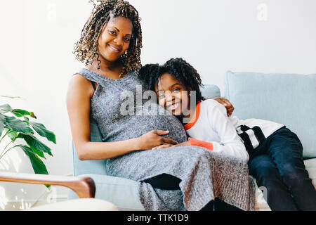 Portrait von glückliche Tochter umarmen schwangere Mutter beim Sitzen auf dem Sofa zu Hause Stockfoto