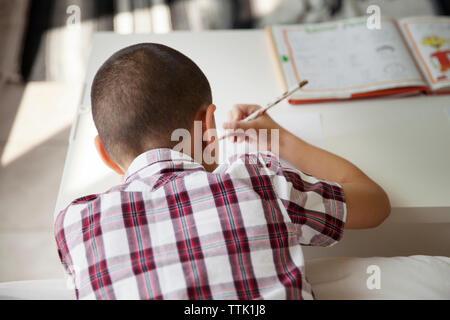 Ansicht der Rückseite des Jungen studieren an der Tabelle im Haus Stockfoto