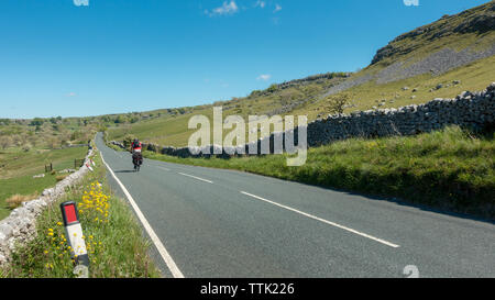 Britische Landschaft: der Mann, der lange Abstand Radfahren auf der Straße Fahrrad mit schwer beladenen Rucksäcke auf der B 6255 in Richtung Norden. Yorkshire Dales Stockfoto