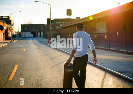 Rückansicht des Menschen skateboard Durchführung beim Gehen auf der Straße in der Stadt Stockfoto