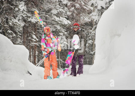 Freunde, Snowboards und Skier beim Stehen auf schneebedeckten Feld Stockfoto