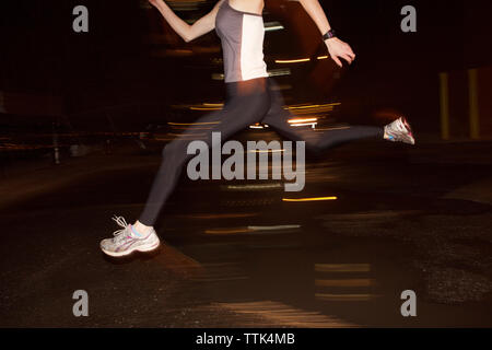 Niedrige Abschnitt der weiblichen Jogger springen über Pfütze in der Stadt bei Nacht Stockfoto