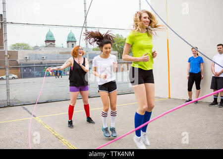 Freunde bei Frauen double Dutch gegen Zaun suchen Stockfoto