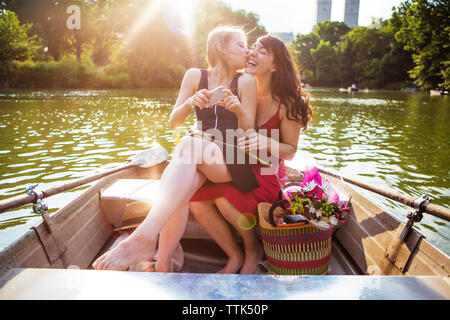 Frau küssen Freundin unterwegs im Boot auf dem See Stockfoto