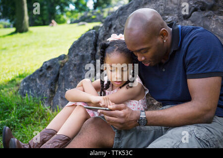 Vater und Tochter suchen Bei digital Tablet im Park Stockfoto