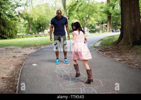 Mädchen spielen Hopse mit Vater auf der Straße am Park Stockfoto