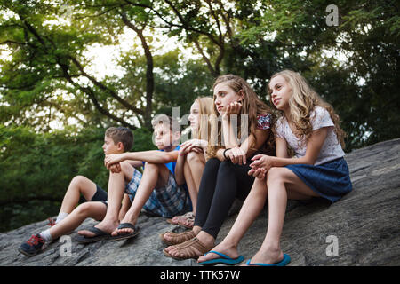 Low Angle View der Geschwister sitzen auf Rock gegen Bäume im Park Stockfoto