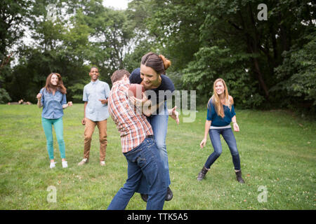 Mann verteidigenden Frau mit Fußball-Ball, während Freunde sie beobachten auf Feld Stockfoto