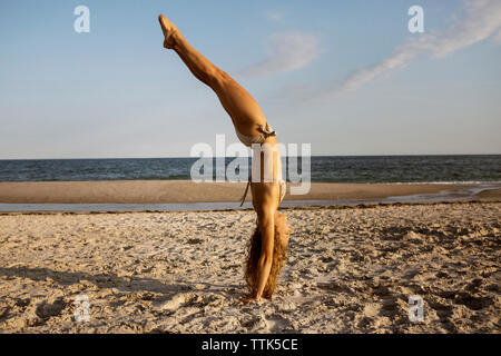 Seitenansicht der Frau macht handstand am Strand gegen Sky Stockfoto