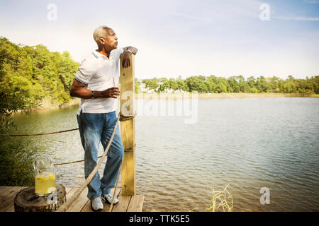 Nachdenklich älterer Mann stand auf Pier am See gegen Sky Stockfoto