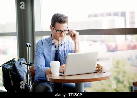 Geschäftsmann, der am Laptop arbeitet, während er in der Cafeteria an der U-Bahn-Station sitzt Stockfoto