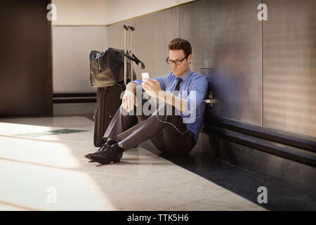 Geschäftsmann, der das Smartphone auflädt, während er auf dem Boden an der U-Bahn-Station sitzt Stockfoto