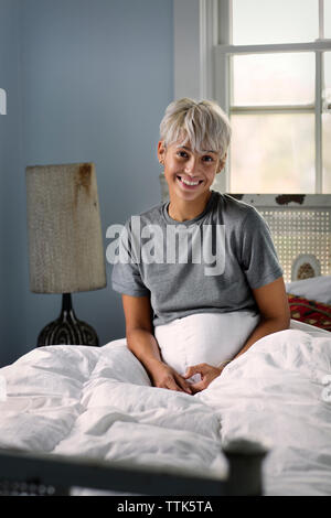 Porträt der glückliche junge Frau sitzt auf dem Bett zu Hause. Stockfoto