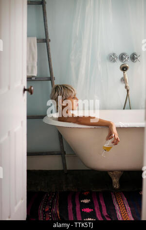 Seitenansicht der nachdenkliche Frau mit Getränke Glas beim Entspannen in der Badewanne zu Hause Stockfoto