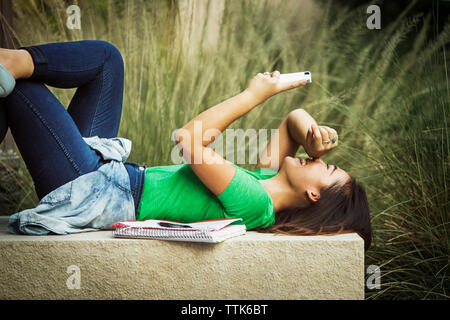 Glückliche Frau mit Handy beim Lügen auf konkrete Sitzbank Stockfoto