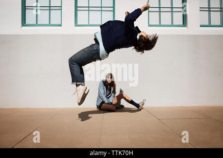 Mann tun, Salto, während Frau gegen Wand saß Stockfoto
