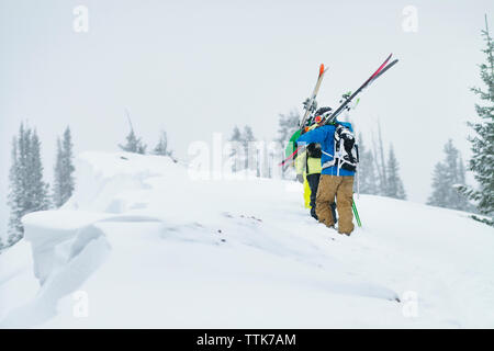 Ansicht der Rückseite des Freunde Skier tragen beim Gehen auf Schnee bedeckten Berg Stockfoto