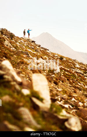 Fernsicht auf Wanderer, der auf etwas zu Freund beim Stehen auf Berg mit Hund Stockfoto