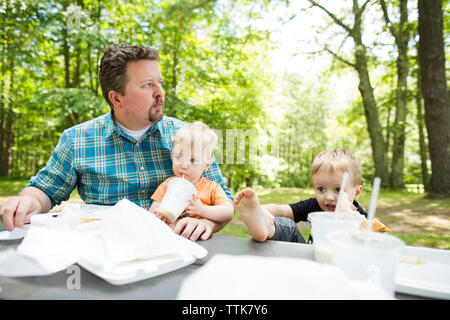 Vater mit Söhnen im Picnic Tisch sitzt im Park Stockfoto