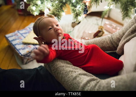 Baby Mädchen mit Bogen und Rot sieht bei Mama neben dem Weihnachtsbaum Stockfoto