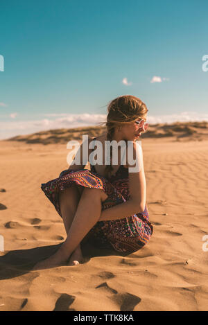 Frau mit Sonnenbrille auf Sand am Strand gegen den blauen Himmel während der sonnigen Tag Stockfoto