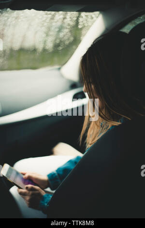 Seitenansicht der Frau mit Handy unterwegs im Auto. Stockfoto