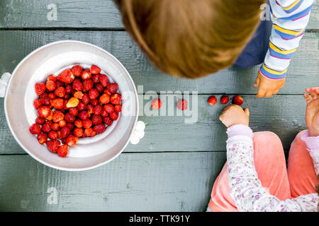 Ansicht von oben der Geschwister spielen mit frisch geernteten Erdbeeren auf Diele Stockfoto