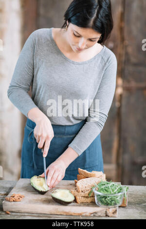 Frau schneiden Avocado auf hölzernen Tisch zu Hause Stockfoto