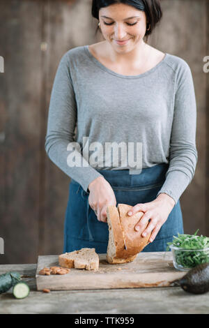 Frau schneiden Brot auf hölzernen Tisch zu Hause Stockfoto