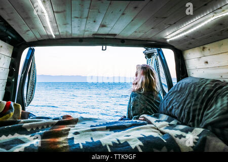 Ansicht der Rückseite Frau suchen auf See während lehnte sich gegen Travel trailer Stockfoto