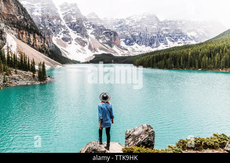 Ansicht der Rückseite Frau in hat zu betrachten und stehen auf Rock von Moraine Lake im Banff National Park Stockfoto