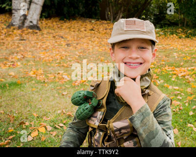 Portrait von Süß lächelnde junge tragen Armee Soldat Kostüm beim Sitzen auf der Wiese im Park Stockfoto