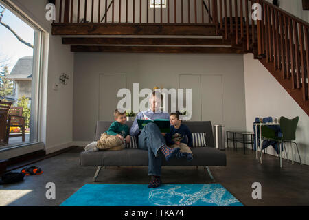 Vater mit Söhnen während Buch auf dem Sofa zu Hause sitzen Stockfoto