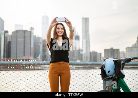 Frau unter selfie beim Stehen mit dem Fahrrad gegen den Fluss in der Stadt Stockfoto