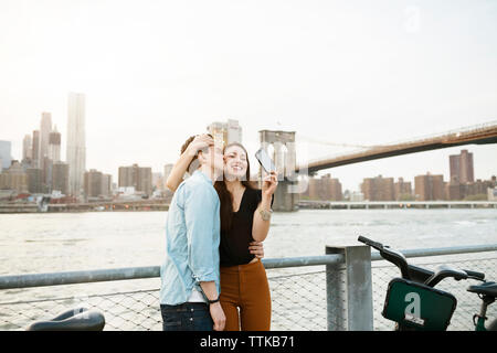 Mann küssen glücklich Frau fotografieren gegen East River in der Stadt Stockfoto