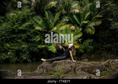 Seitenansicht der Frau entspannend auf Felsen am Seeufer in El Yunque National Forest Stockfoto