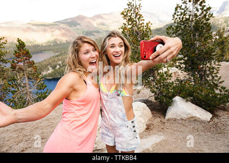 Gerne weibliche Freunde unter selfie mit Handy beim Stehen auf Berg im Wald Stockfoto