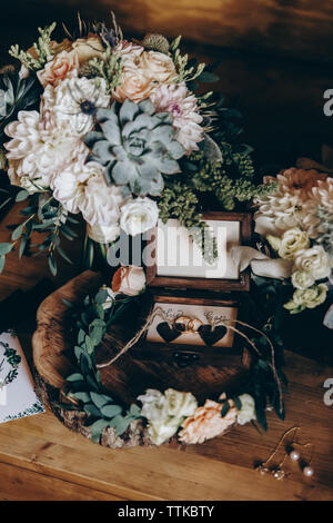 In der Nähe der Hochzeit Ringe inmitten Kranz von Blumenstrauß auf dem Tisch Stockfoto