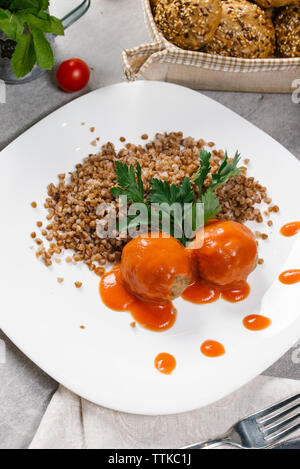 Hohe Betrachtungswinkel von gekochten Buchweizen mit Fleischbällchen und Tomatensauce in der Platte am Tisch serviert Stockfoto