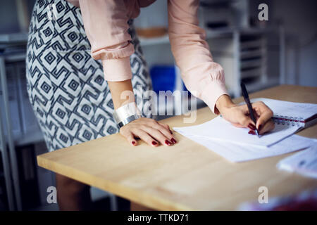 Mittelteil der Geschäftsfrau schreiben in Tagebuch am Schreibtisch im Büro Stockfoto