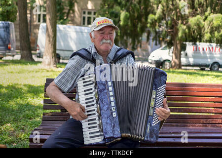 Zemun, Serbien, 16. Juni 2019: Portrait eines reifen Mann mit Schnurrbart auf einer Bank sitzen und spielen Mundharmonika Stockfoto