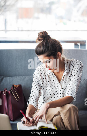 Geschäftsfrau schreibt im Tagebuch, während sie im Restaurant auf dem Sofa sitzt Stockfoto
