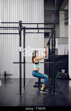 Seitenansicht des weiblichen Athleten trainieren mit Gymnastik Ringe in Health Club Stockfoto