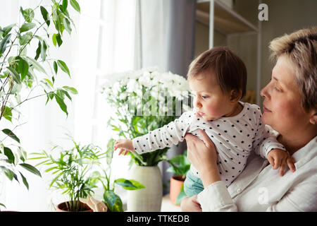 Reife Frau mit Baby Mädchen, während man durch die Fenster zu Hause Stockfoto