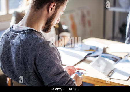 Mann mit Smart Phone beim Sitzen am Tisch im Klassenzimmer Stockfoto