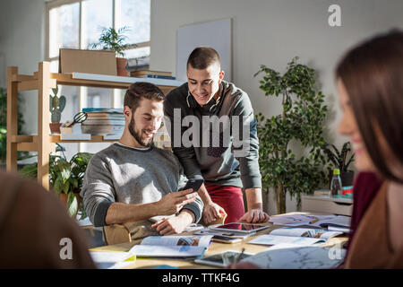 Freunde mittels Smart Phone beim Sitzen am Tisch im Klassenzimmer Stockfoto