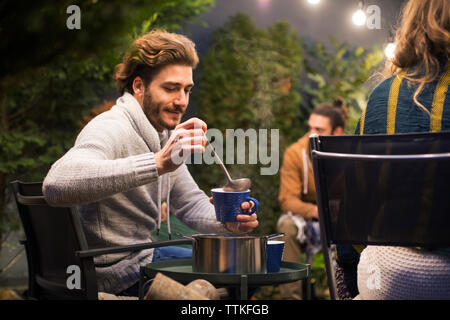 Man gießt Drink in Schale beim Sitzen mit Freunden im Hinterhof Stockfoto